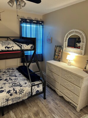 A bunk bed with a decorative headboard, a dresser with a mirror, and a window with blinds. - Cozy 2-bedroom condo in Gulf Shores with AC (Gulf Shores)