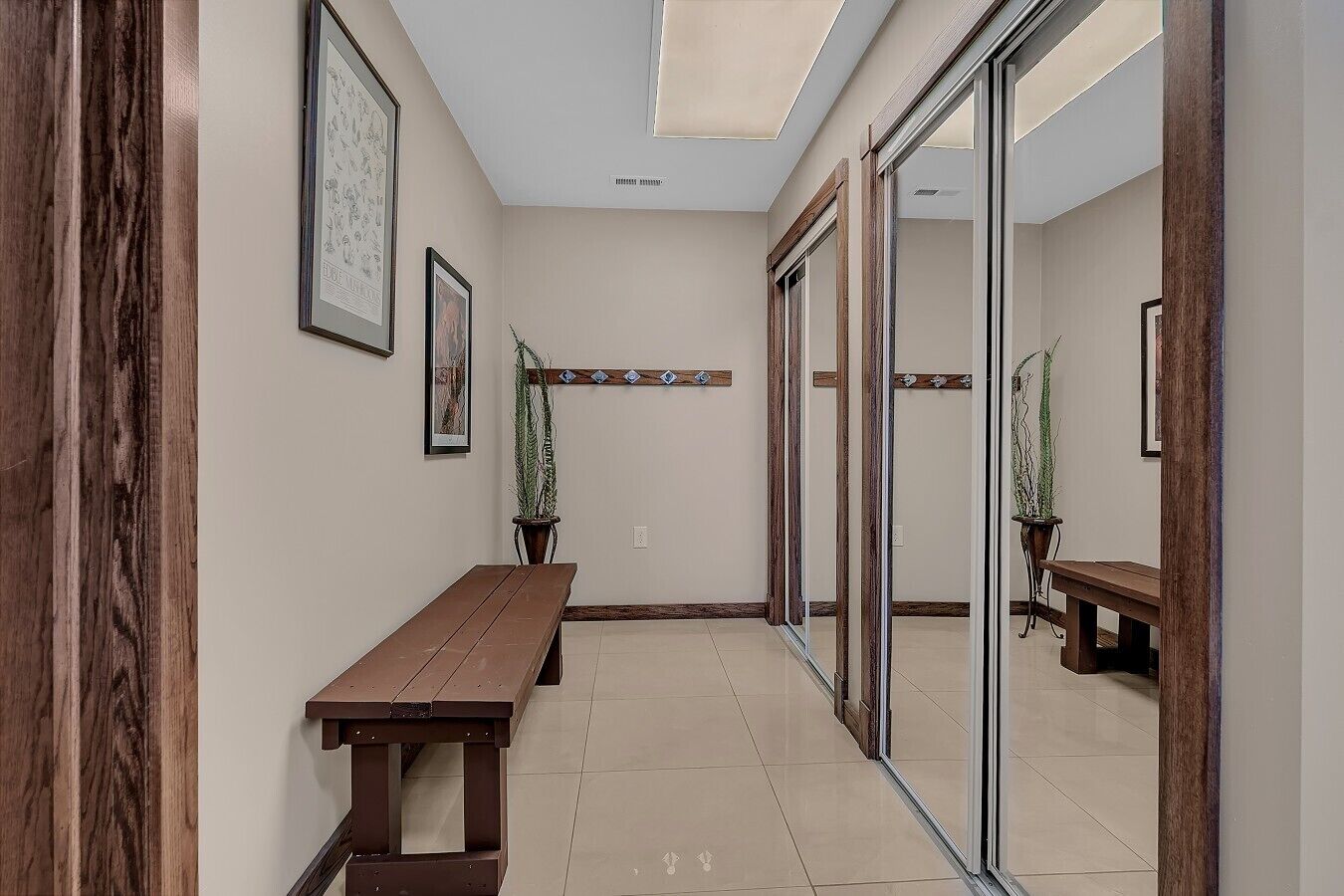 A hallway with a wooden bench, framed artwork, potted plants, and a glass door.