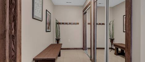 A hallway with a wooden bench, framed artwork, potted plants, and a glass door.