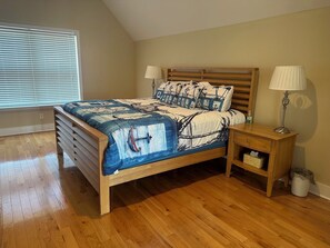 A bedroom with a wooden bed, two bedside lamps, a nightstand with a lamp, and a window with blinds. - Pelican Point (Carrabelle)