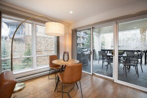 A modern room with a dining table, chairs, a lamp, and large windows. - Luxe 3BR in Village, Hot Tub, Pool, Sauna, Parking (Vail)