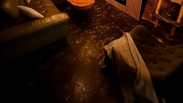Tunnelmallinen huone, jossa on kiviseinä, nahkasohva, puinen sohvapöytä ja seinälle asennettu litteänäyttöinen televisio.