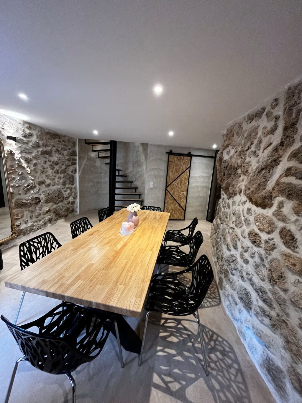 Un salón de conferencias con una mesa de madera, sillas negras, paredes de piedra y una escalera.