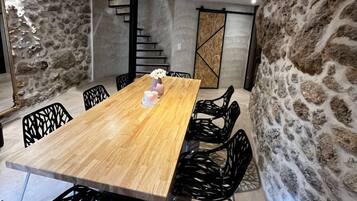 Un salón de conferencias con una mesa de madera, sillas negras, paredes de piedra y una escalera.