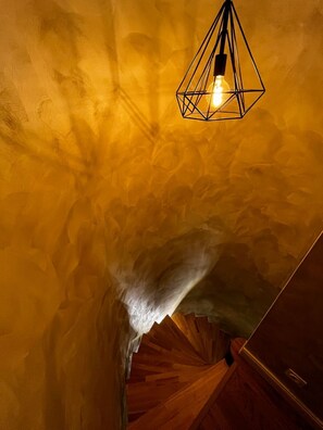 A room with a textured yellow wall, a wooden staircase, and a hanging light fixture.