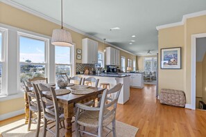 A spacious kitchen with a central island, large windows, and a dining area with a wooden table and chairs. - Peaceful Marshfront Retreat w/ Water Views, Walk to Beach, 4BR (Atlantic Beach)