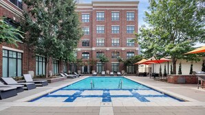A swimming pool with lounge chairs and umbrellas, surrounded by brick buildings and trees. - The Metro by Stylish Stays (Tulsa)