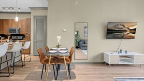 A modern kitchen with a microwave, dining area with chairs and a table, a white cabinet, and a painting on the wall. - The Metro by Stylish Stays (Tulsa)