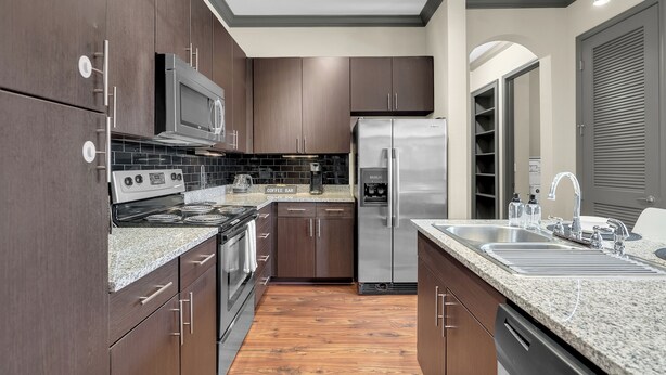 A modern kitchen with dark wood cabinets, stainless steel appliances, granite countertops, and a built-in coffee bar. - The Metro by Stylish Stays (Tulsa)