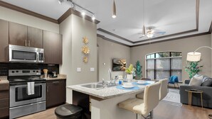 A modern kitchen with a built-in microwave, oven, and sink. There is a dining area with a bar stool and a small table. - The Metro by Stylish Stays (Tulsa)
