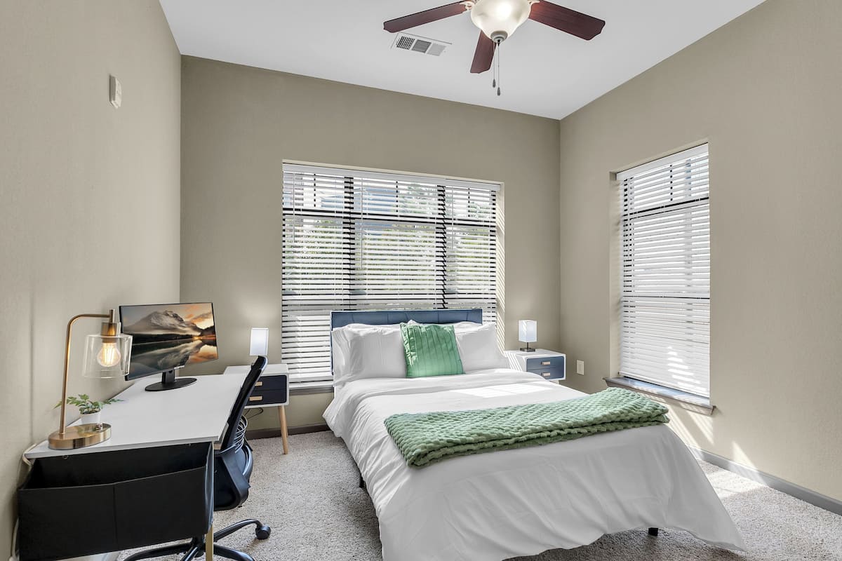 A bedroom with a bed, desk, chair, and ceiling fan.