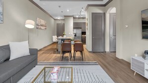 A modern living room with a sofa, a coffee table, and a dining area with chairs and a table. - The Metro by Stylish Stays (Tulsa)