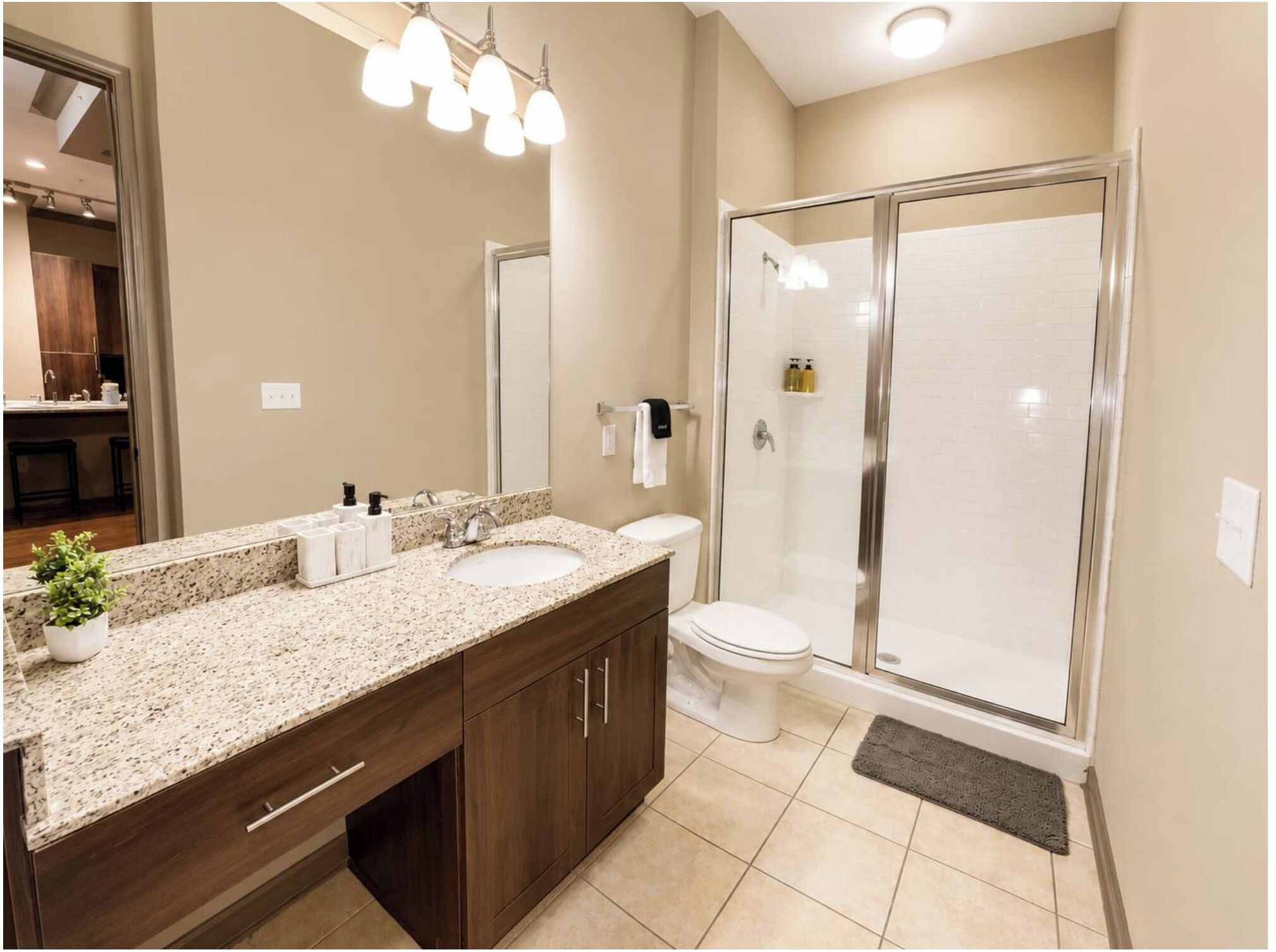A modern bathroom with a granite countertop, dual sinks, a toilet, a glass shower enclosure, and a large mirror.