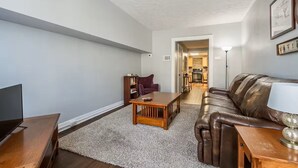 Una sala de estar con un sofá, una mesa de centro, un mueble para televisión y una estantería.