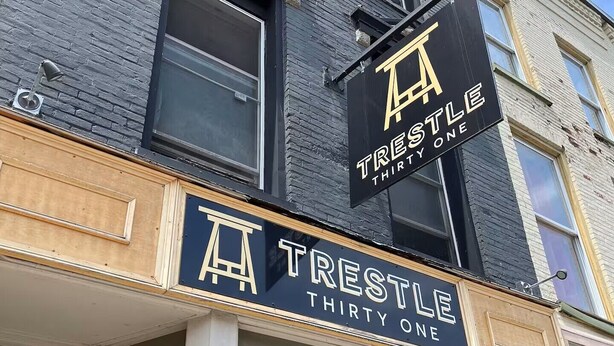 Un edificio con un letrero que dice 'TRESTLE THIRTY ONE' y un gran logotipo en forma de 'T'.