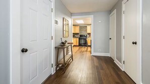 Un pasillo con puertas blancas, suelo de madera y una cocina a lo lejos.