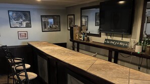 A bar area with a long counter, bar stools, a television mounted on the wall, and framed pictures on the wall. - Pet friendly 3-bedroom. About a mile from downtown. Fenced-in backyard. (Hudson’)
