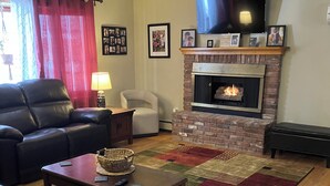 A living room with a fireplace, leather sofa, armchair, and a television mounted on the wall. - Pet friendly 3-bedroom. About a mile from downtown. Fenced-in backyard. (Hudson’)