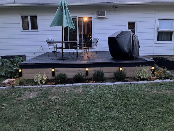 A deck with outdoor furniture, a covered grill, and string lights.