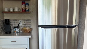 A kitchen with a stainless steel refrigerator, a white cabinet, a coffee maker, and a shelf with coffee creamer bottles. - Delightful 3-bedroom Spanish inspired house in Richmond. The Rustic Villa. (Richmond)