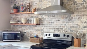 A kitchen with white cabinets, a stainless steel stove, a microwave, and a brick backsplash. - Delightful 3-bedroom Spanish inspired house in Richmond. The Rustic Villa. (Richmond)