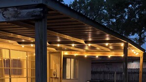 A covered patio area with a wooden bench and table, surrounded by a wooden deck and a garden bed with pebbles. - Delightful 3-bedroom Spanish inspired house in Richmond. The Rustic Villa. (Richmond)