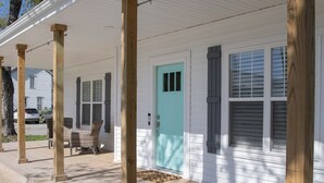 Une maison blanche avec un porche, des colonnes en bois et une porte bleue.