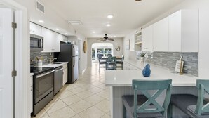 A modern kitchen with white cabinets, a central island, and a dining area with teal chairs. - Waterfront Home with Dockage & 
 Steps to Cabana Club (Key Colony Beach)