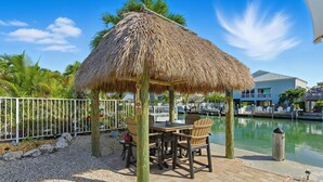 A thatched-roof outdoor seating area with a view of a marina and buildings. - Waterfront Home with Dockage & 
 Steps to Cabana Club (Key Colony Beach)