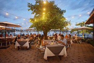 Un área de comedor al aire libre con mesas, sillas, luces colgantes y sombrillas.