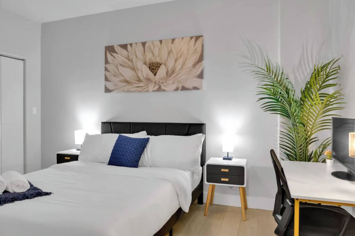 A modern bedroom with a bed, bedside tables, a desk, and a large plant.