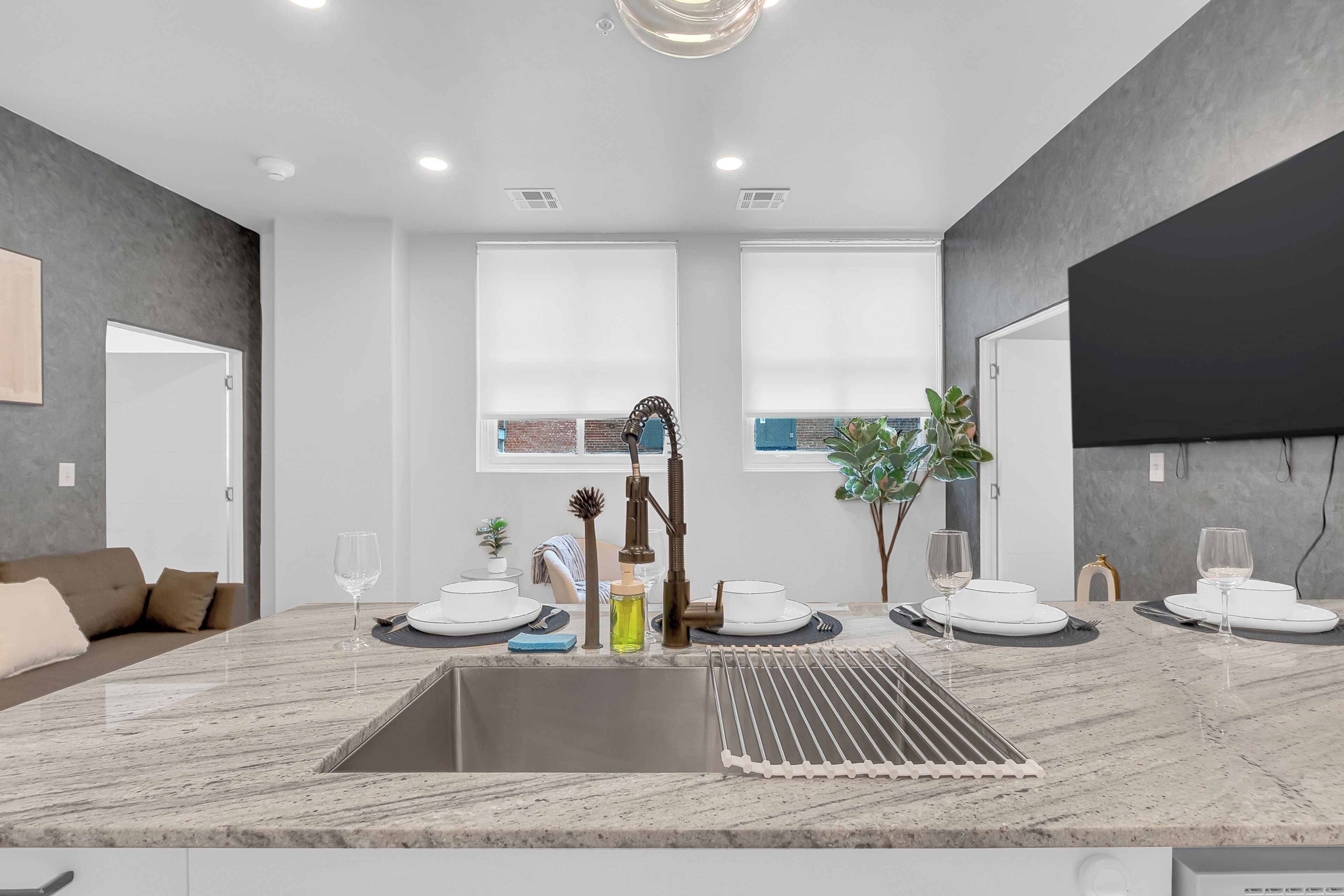 A modern kitchen with a marble countertop, a sink, and a dining area with white plates and glasses.