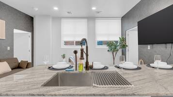A modern kitchen with a marble countertop, a sink, and a dining area with white plates and glasses.