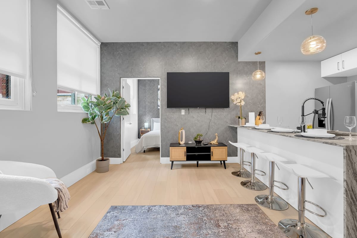 A modern kitchen with a flat-screen TV, bar stools, and a potted plant.