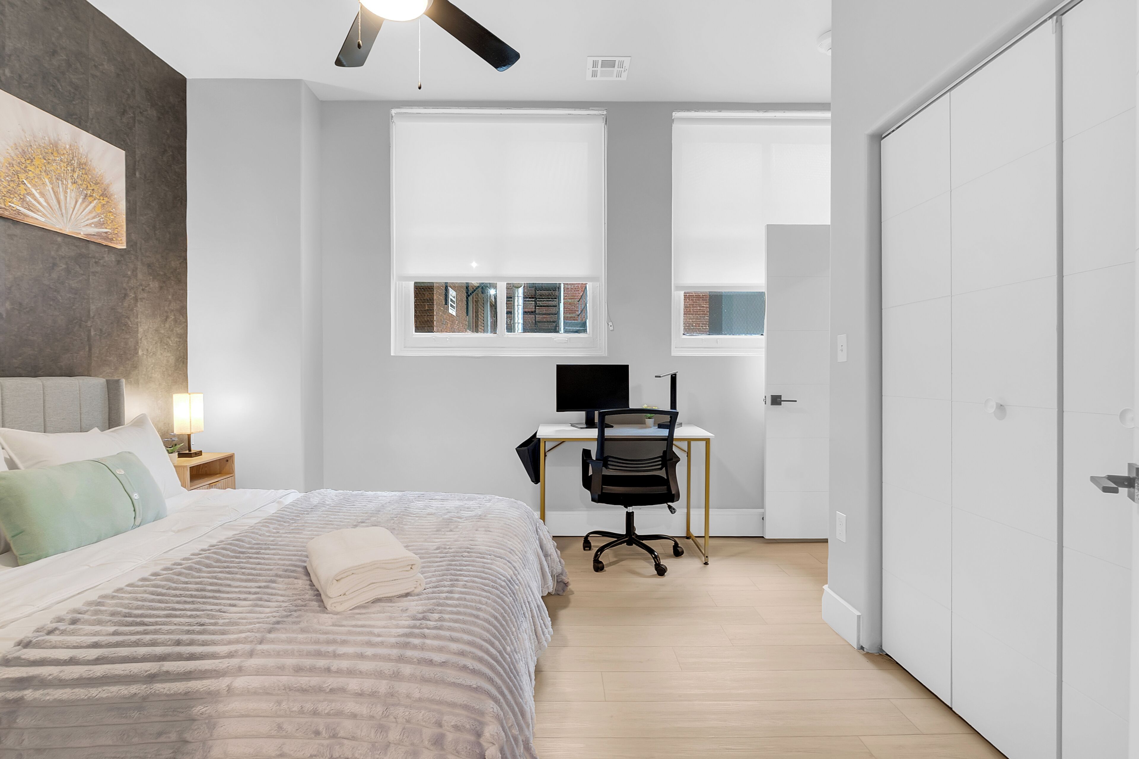 A bedroom with a bed, a desk with a computer, a chair, and a wardrobe.