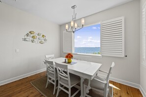 A dining area with a white table, chairs, a chandelier, and a view of the sea through a window with white shutters. - TOP FLORIDA's Villa Porpoise Point (Cape Coral)