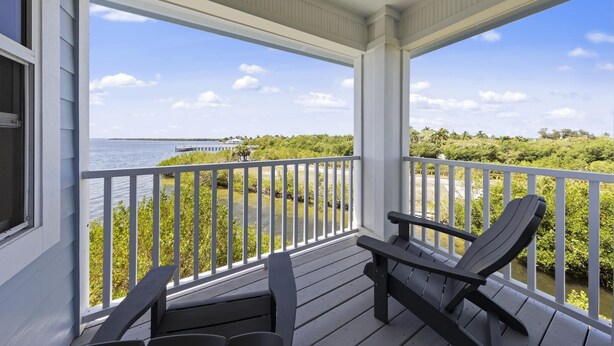 A covered porch with two Adirondack chairs, a view of the water, and a distant pier. - TOP FLORIDA's Villa Porpoise Point (Cape Coral)