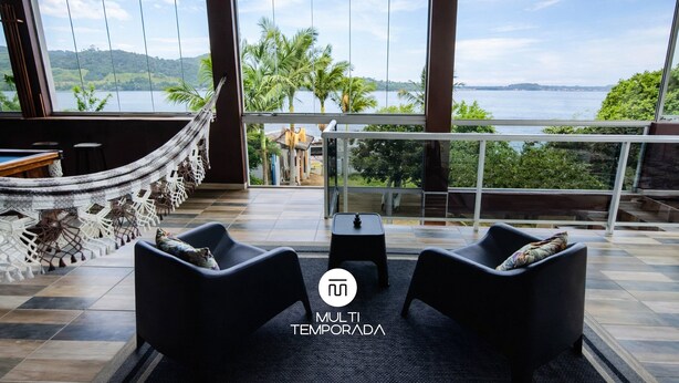 A room with a large window, a hammock, two sofas, and a small table. - Casa na Lagoa Imaruí-SC (Imaruí)