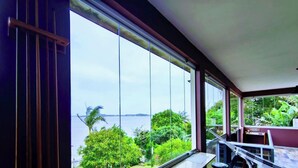 A room with large windows, a balcony, and a view of the sea and greenery. - Casa na Lagoa Imaruí-SC (Imaruí)