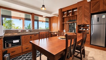 Cocina moderna con armarios de madera, un refrigerador de acero inoxidable y una zona de comedor con mesa y sillas de madera.