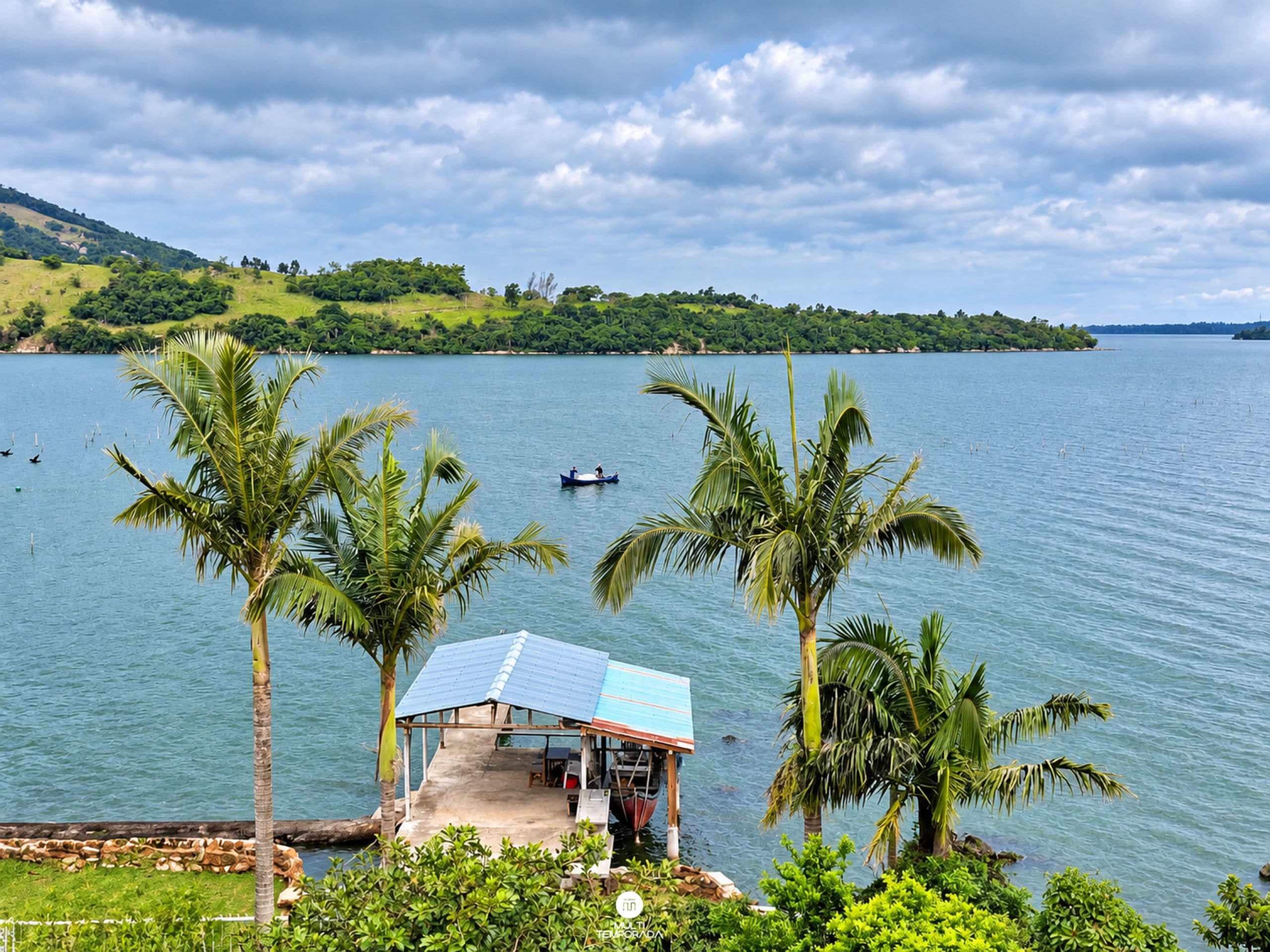 A small house with a roof and a dock extending into a calm lake, surrounded by palm trees and a hilly landscape.