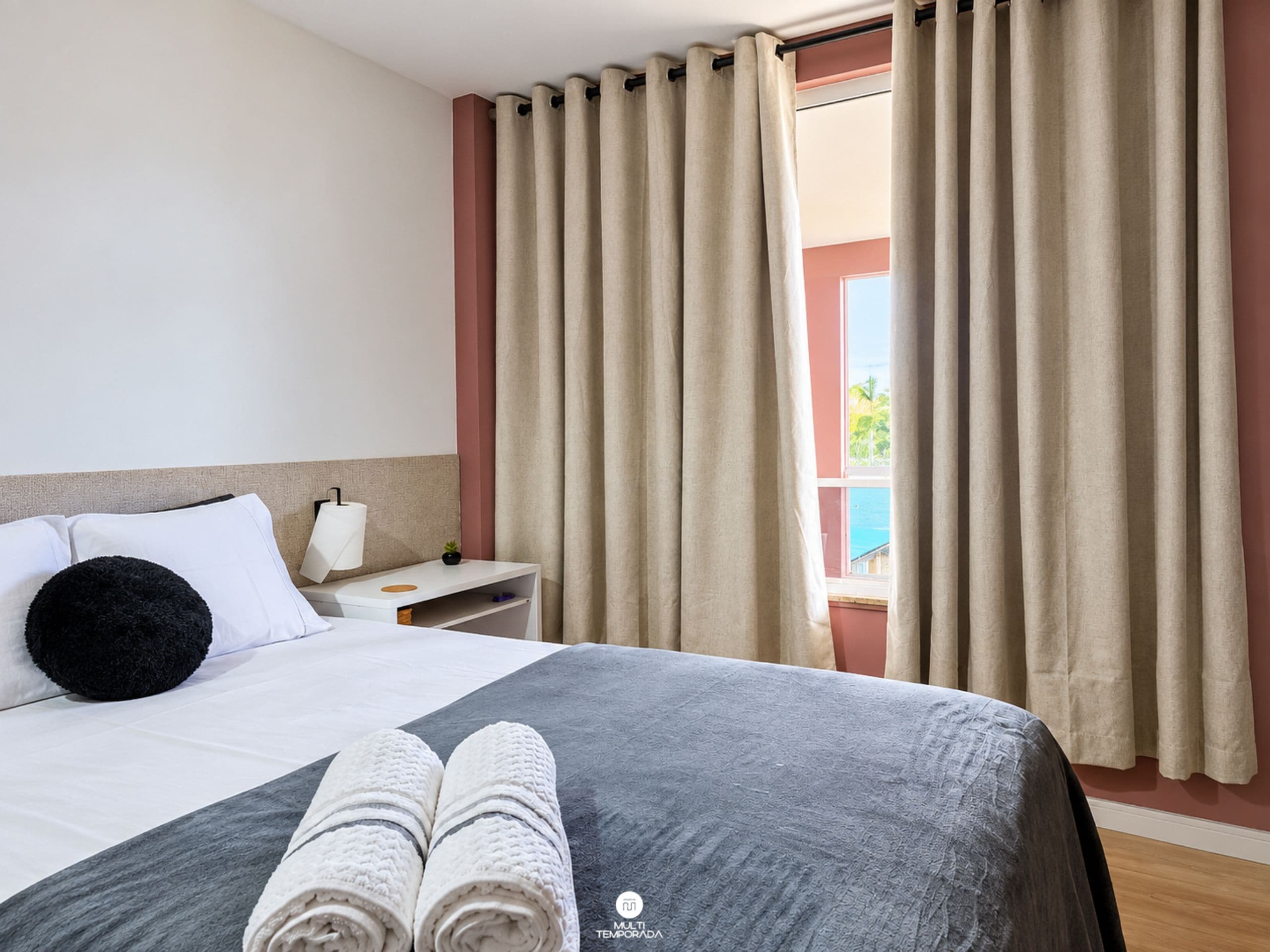 A hotel room with a bed, a nightstand, a lamp, and a window with curtains.