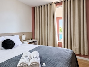 Een hotelkamer met een bed, een nachtkastje, een lamp en een raam met gordijnen.