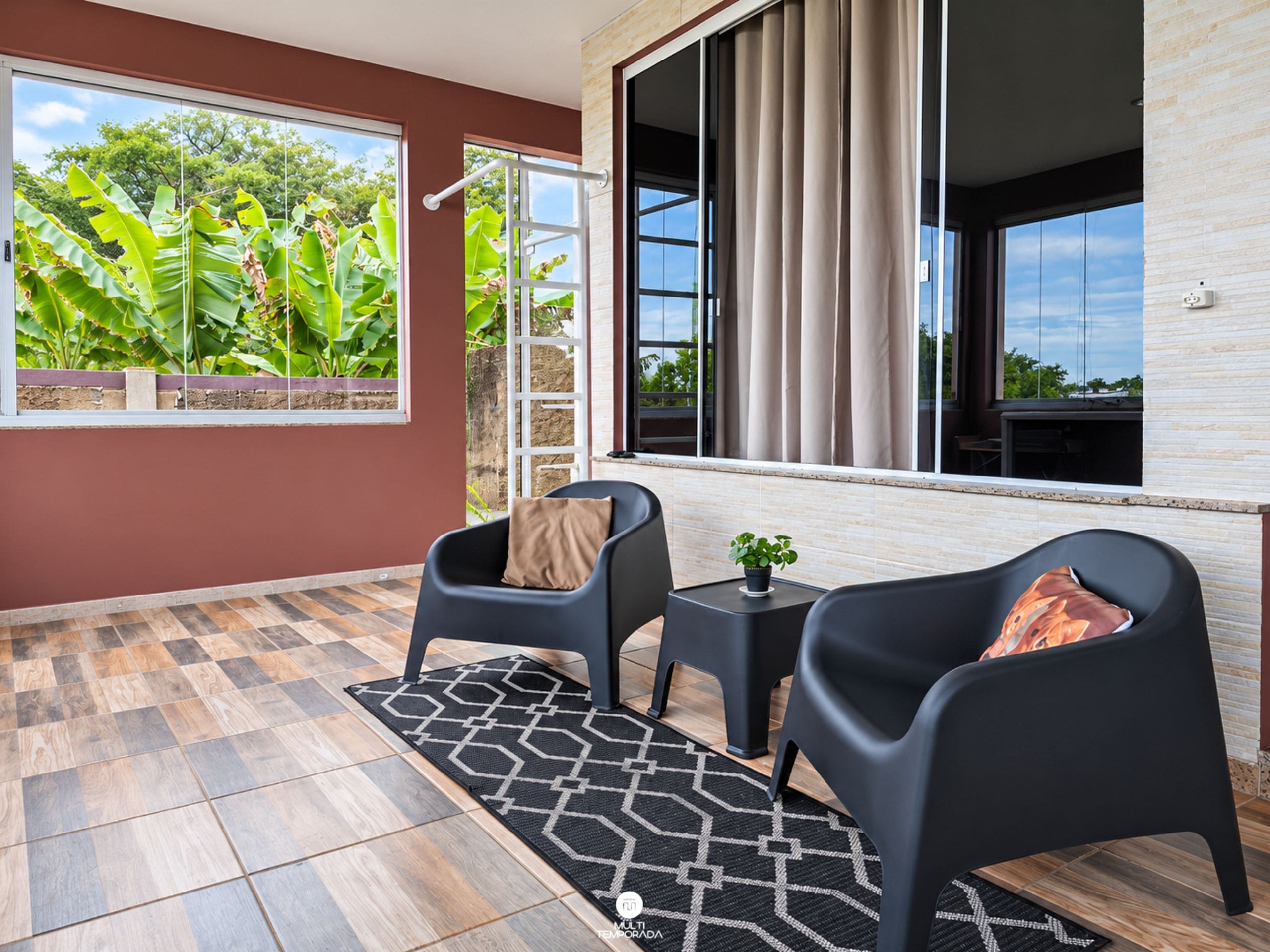 A modern room with a large window, a black sofa, a small table, and a patterned rug.