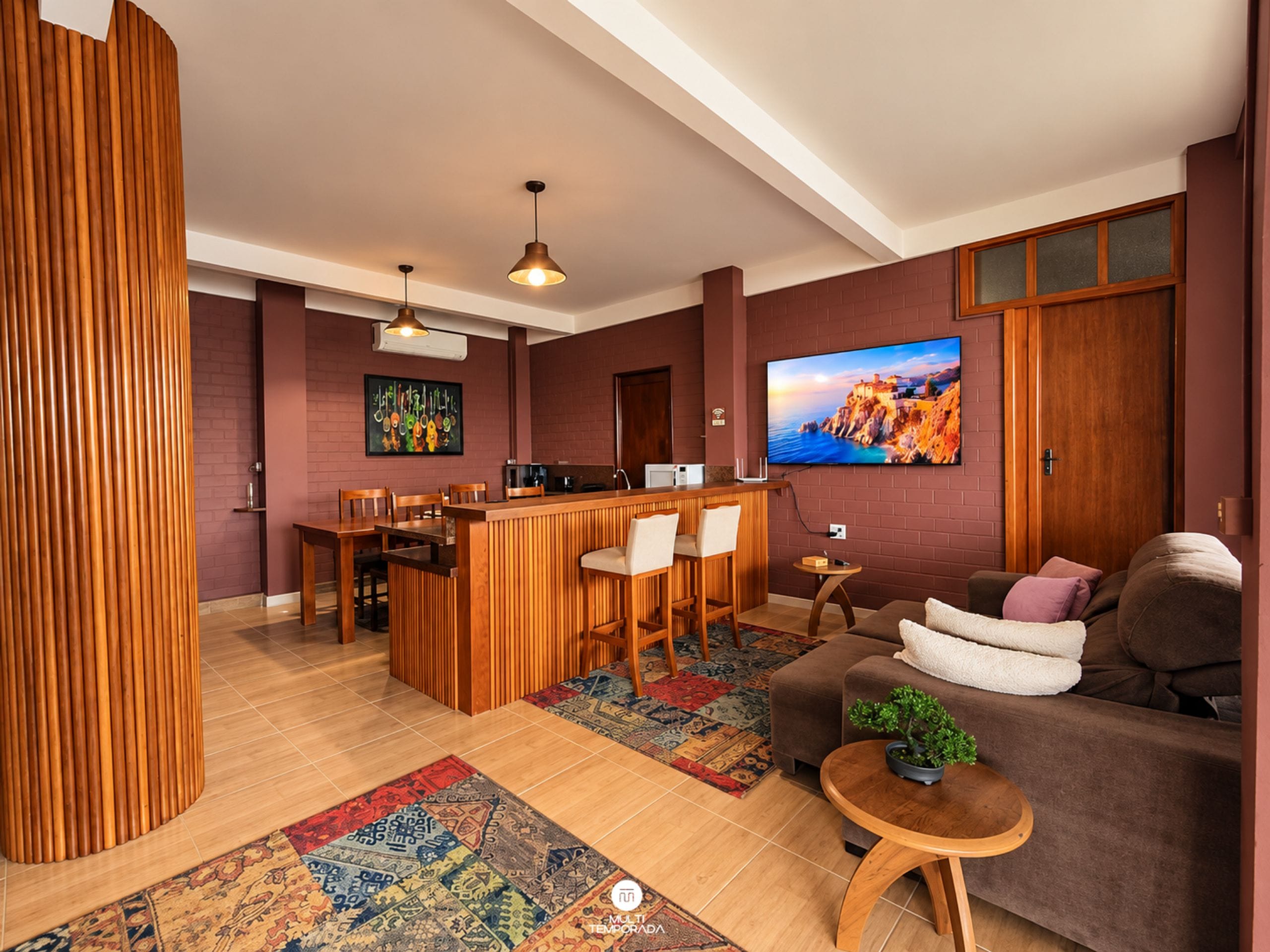 Un salon moderne doté d’un bar en bois, d’un coin salon et d’un téléviseur à écran plat fixé au mur.