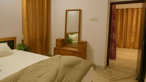 A hotel room with a bed, a dresser, a mirror, and a door leading to another room. - 2-bedroom apartment in perfect Patna with cool AC (Patna)