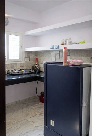 Una cocina con encimera de mármol, estufa a gas, refrigerador y ventana con diseño de cuadrícula.