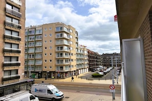 A multi-story residential building with balconies, a van parked in front, and a clear sky.