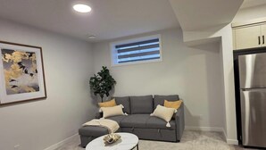 Ein Wohnzimmer mit grauem Sofa, einem kleinen weißen Tisch und einem großen Kühlschrank.