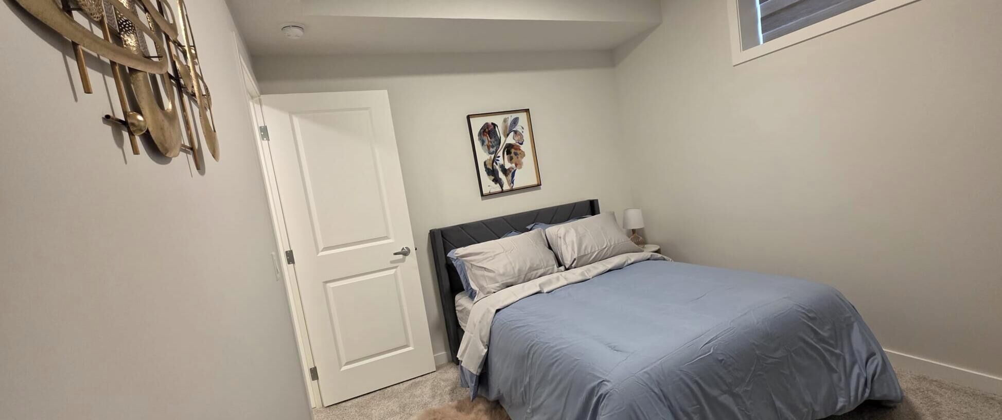 A bedroom with a bed, a door, and a wall-mounted artwork.